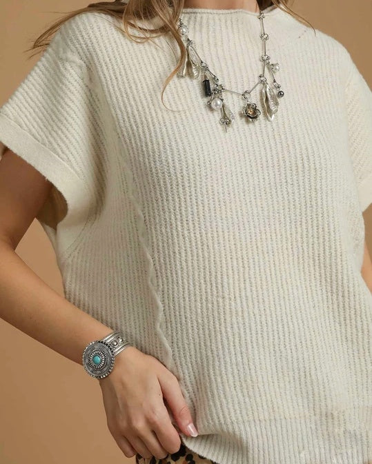 woman wearing a textured white sweater with a silver necklace and bracelet on a beige background