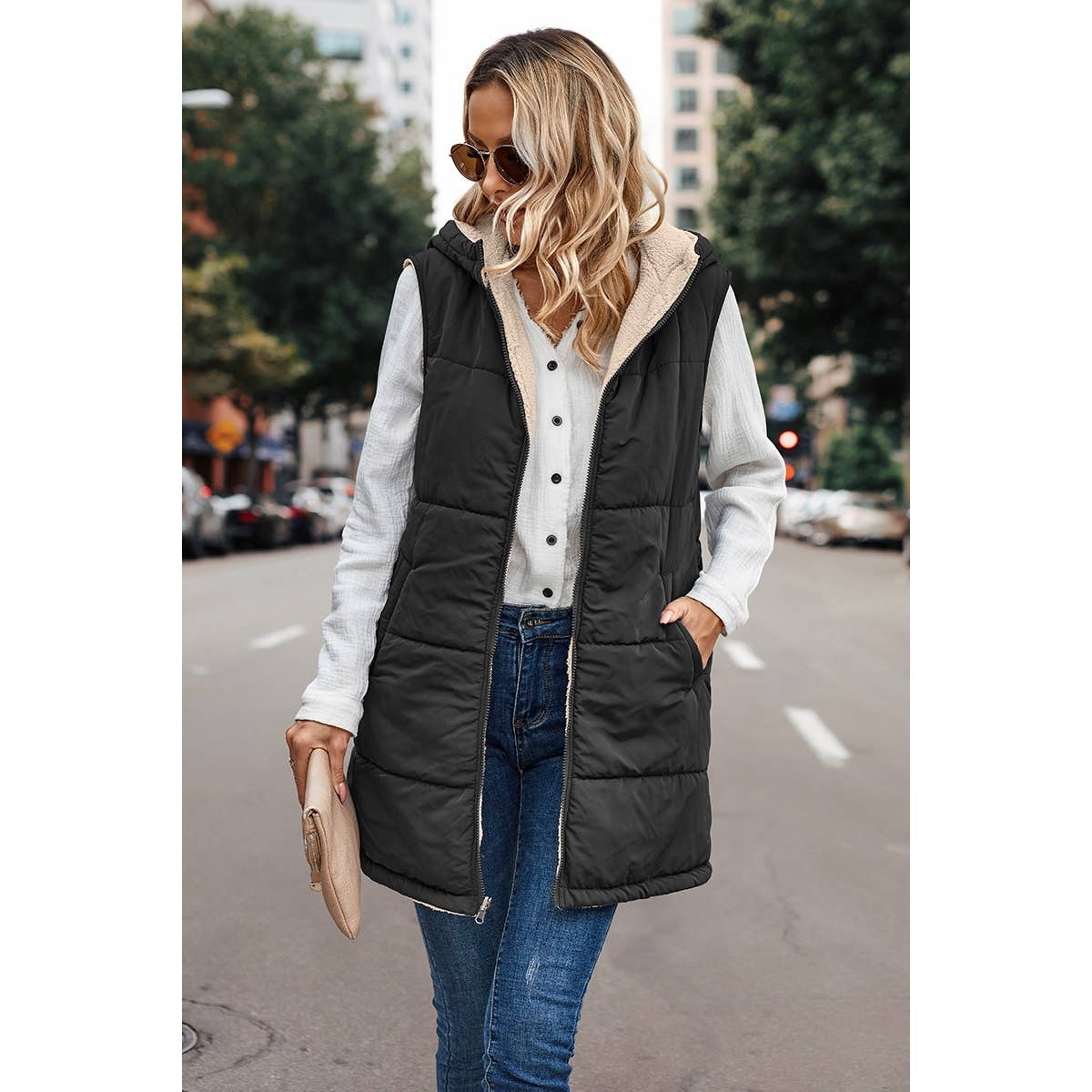 Woman wearing a black puffer vest over a white shirt on a city street.
